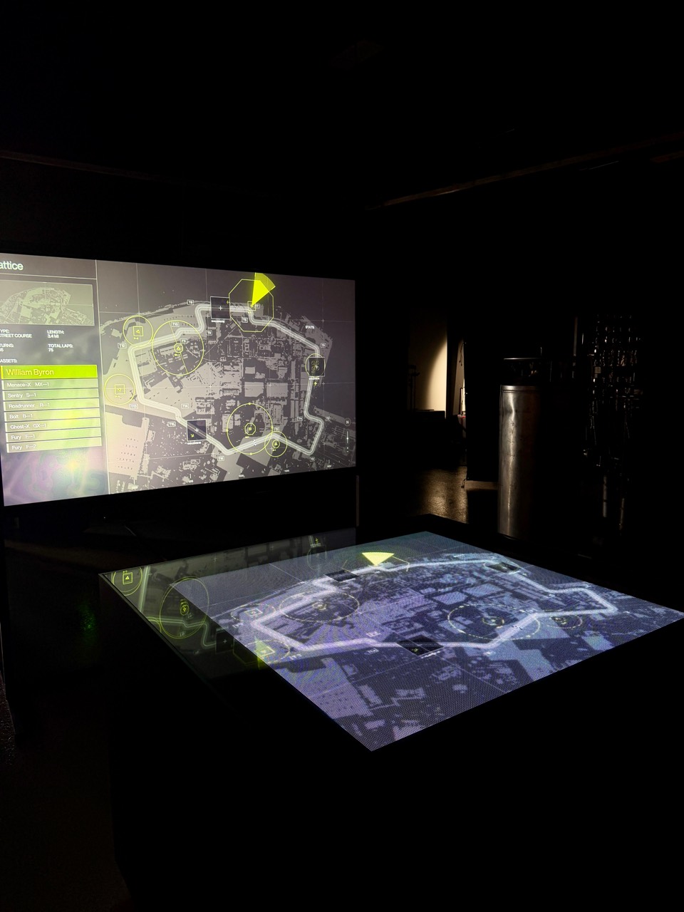 Projected map graphics on a tabletop and wall display in a dark room